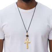 Ankh pendant necklace on a black cord worn by a person in a white shirt.
