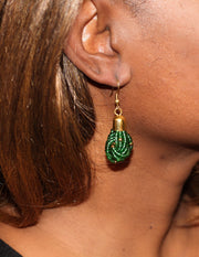 A woman wearing a green beaded earring with gold accents