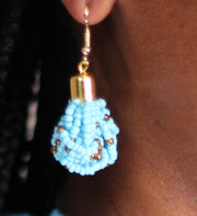 A woman wearing a hand beaded light blue earring with gold accents.