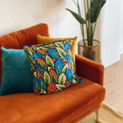 Colorful patterned pillow on an orange couch with a plant in the background