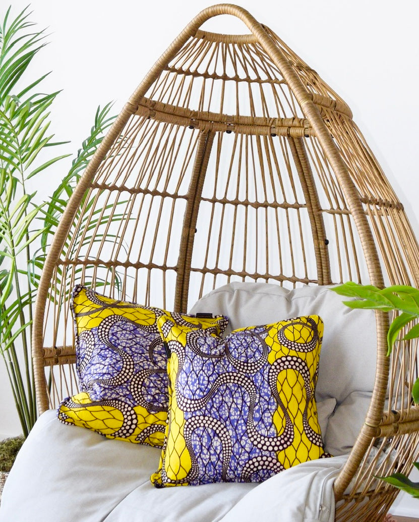 Wicker hanging chair with colorful pillows and a plant in the background