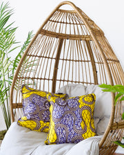 Wicker hanging chair with colorful pillows and a plant in the background
