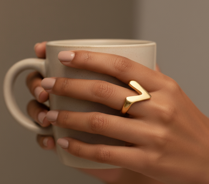 Hand holding a white mug with a gold ring on a neutral background