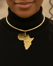 Woman wearing a black turtleneck and gold necklace with an African design in a blurred indoor setting