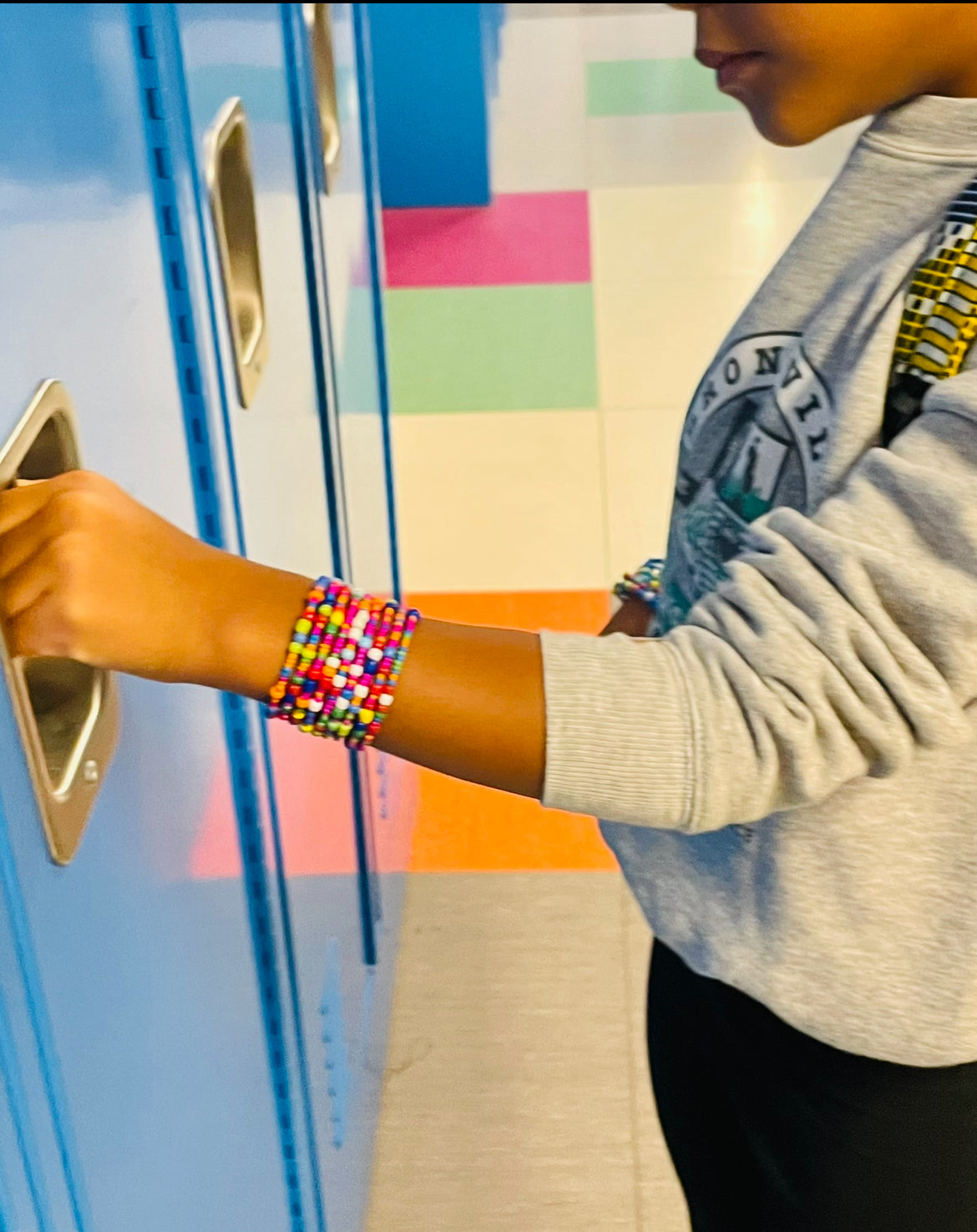 A kid wearing a colorfully beaded wrap bracelet in a school setting.