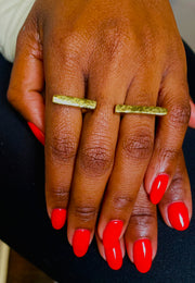 A person wearing a gold-colored hammered ring on their finger, with a visible manicured nail.