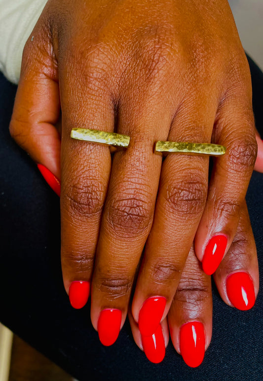 A person wearing a gold-colored hammered ring on their finger, with a visible manicured nail.