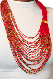 A woman wearing a red braided beaded necklace with black, gold, and yellow accents.