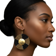 Woman wearing large black and gold beaded earrings on a white background
