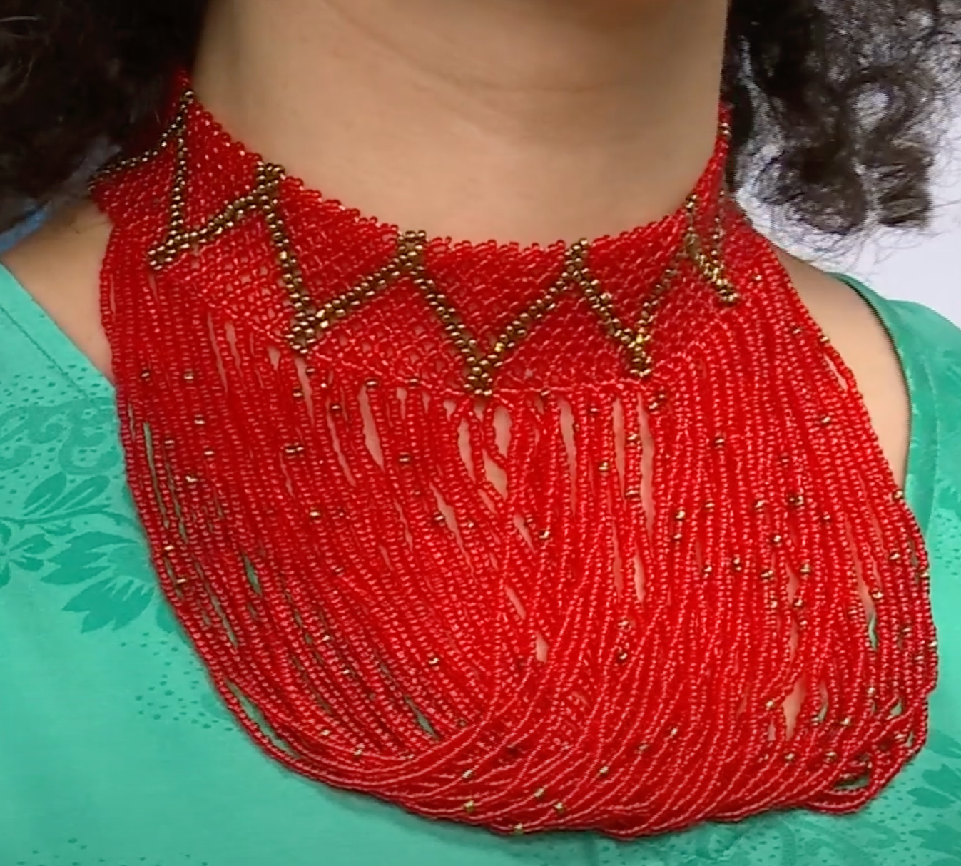 A woman wearing a red beaded choker necklace with gold accents.