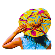 A back view of a woman wearing a colorfully patterned yellow and pink sun hat in a white background.