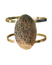 Gold cuff bracelet with a textured oval center on a white background