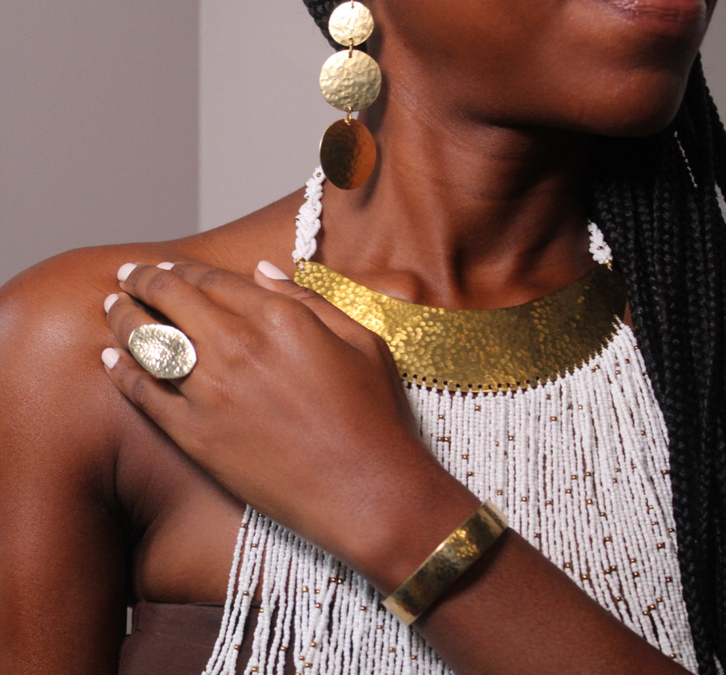 A person's wrist wearing a gold-plated cuff bracelet with a subtle hammered texture.