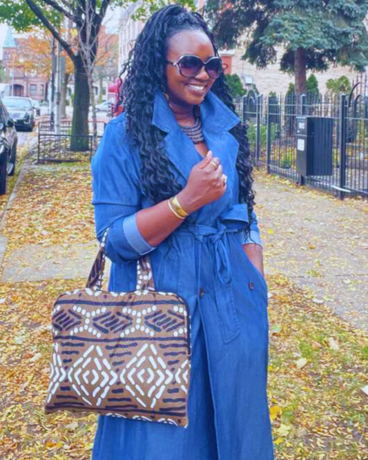 A woman in a blue trench coat holding a patterned laptop bag on a sidewalk.