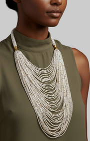 Woman wearing a green sleeveless top with a long, layered necklace against a gray background