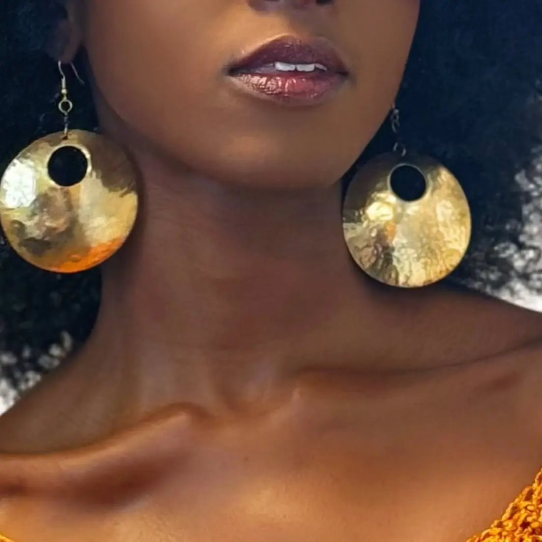 Close-up of a person wearing large gold hoop earrings with a blurred background