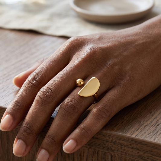 Hand wearing a gold ring on a wooden surface with a neutral background