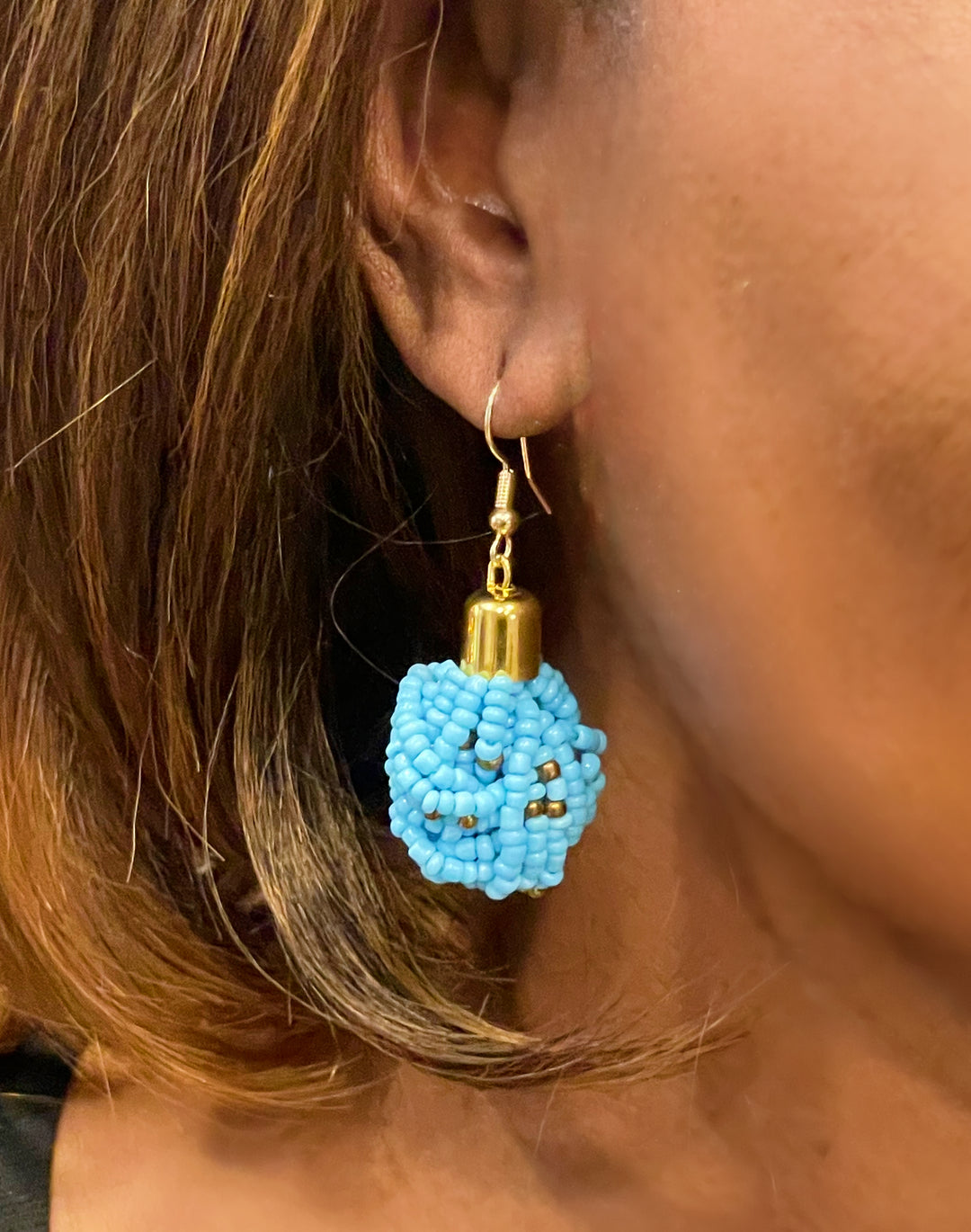 A woman wearing blue beaded earrings with gold accents.