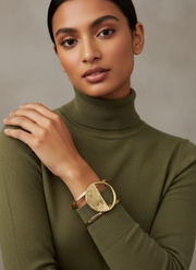 Woman wearing a green turtleneck sweater with a gold bracelet on a neutral background