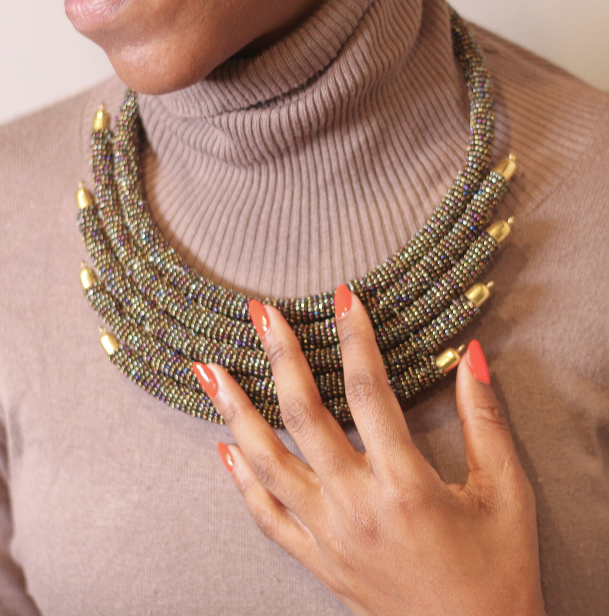 A woman wearing a gold beaded necklace with purple and pink accents.