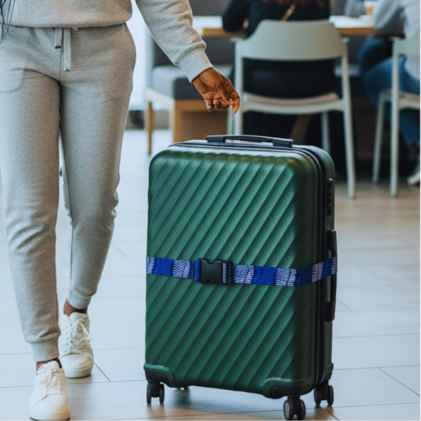 A person walking with a green suitcase with a luggage identifier in an airport terminal.
