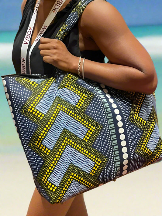 A woman carrying a colorfully patterned yellow and blue tote bag in a beach background.