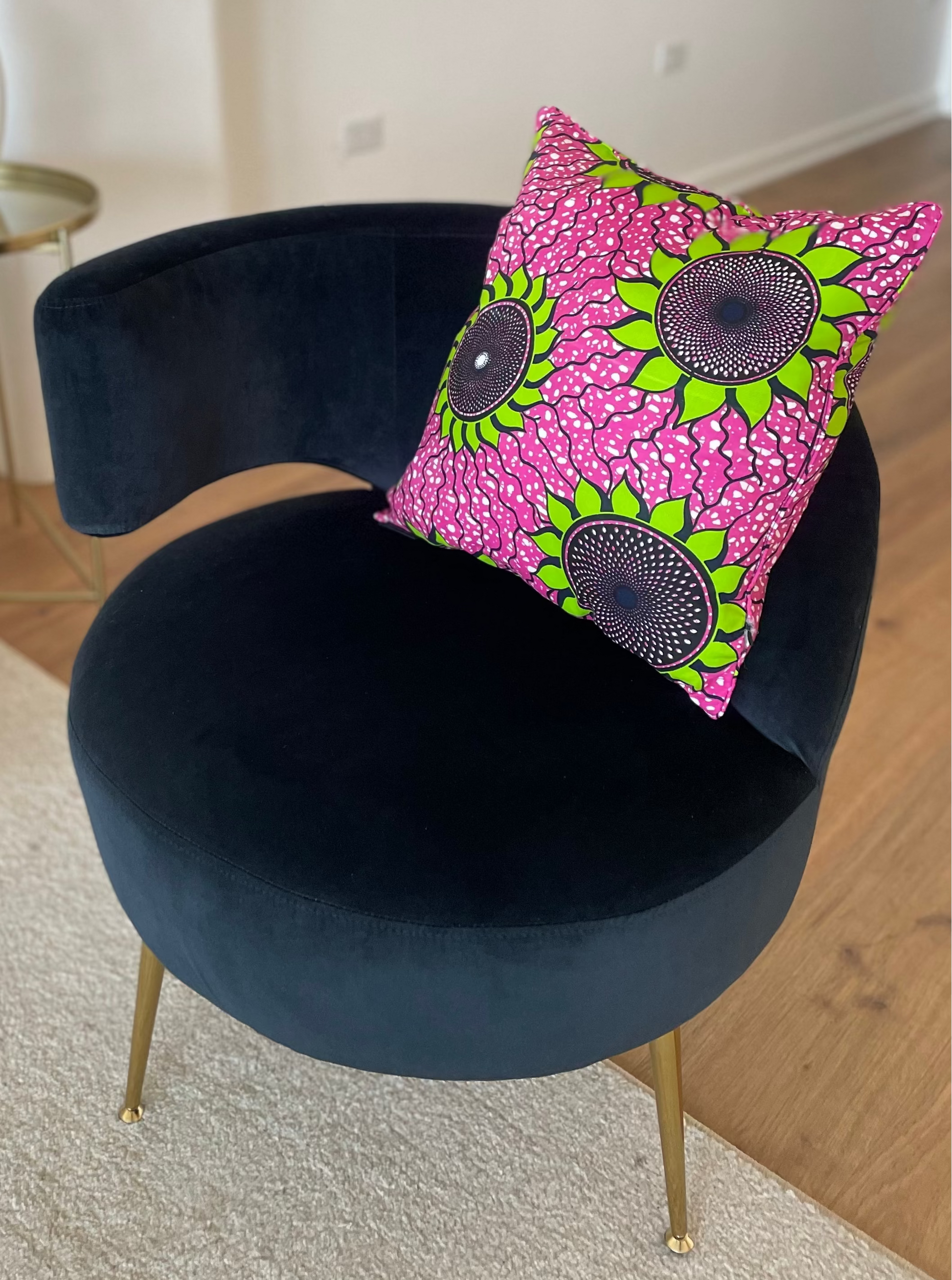 Navy blue chair with a pink and green patterned pillow on a wooden floor.