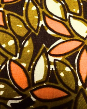 A swatch of fabric with a leaf pattern in green, orange, and white.