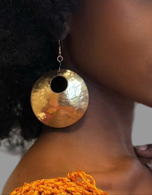 Woman with an afro wearing large gold earrings against a neutral background